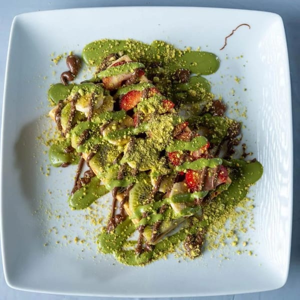 Ranoush dessert with waffles, strawberries, bananas, kiwi, pistachio sauce, and chocolate drizzle.