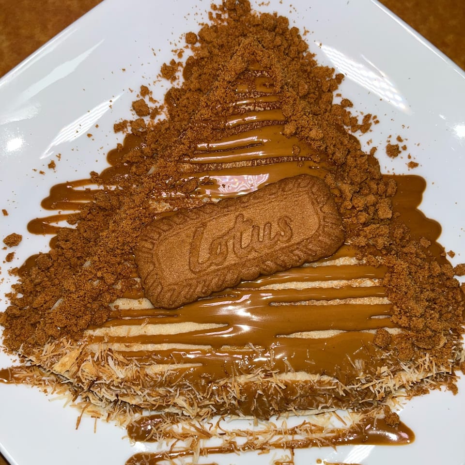 Ranoush dessert with a Lotus Biscoff cookie, crumbled topping, and caramel drizzle on a white plate.