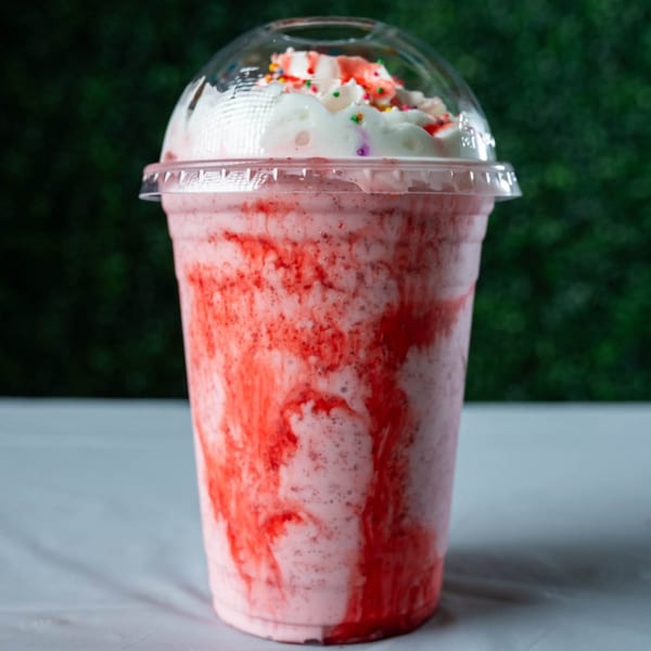Ranoush strawberry milkshake with whipped cream and colorful sprinkles in a clear plastic cup.