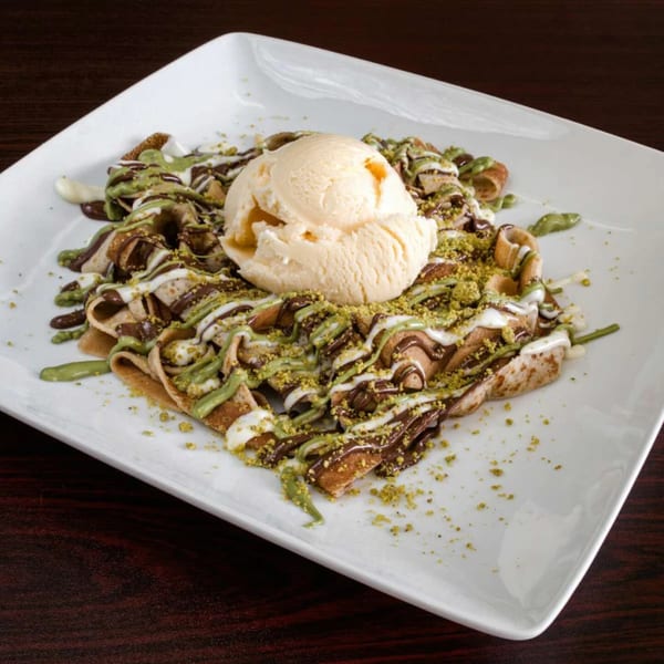 Ranoush dessert crepes drizzled with chocolate, pistachio sauce, and topped with vanilla ice cream.