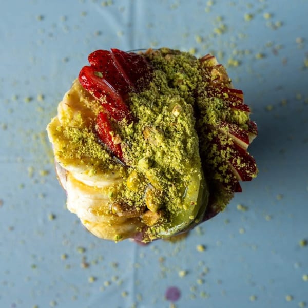 Ranoush dessert with sliced bananas, strawberries, and kiwi, topped with crushed pistachios.