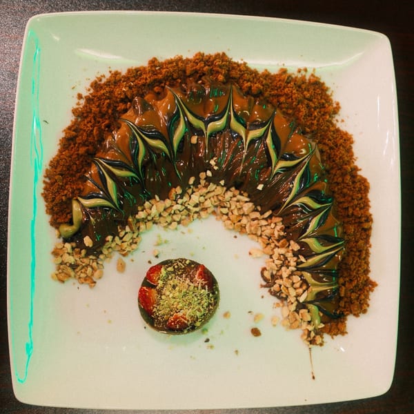 Ranoush dessert with chocolate, green and brown swirls, nuts, cookie crumbs, and a small cake.