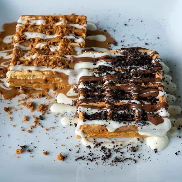 Two Ranoush waffles, one with cookie crumbs and the other with chocolate and cream drizzle.