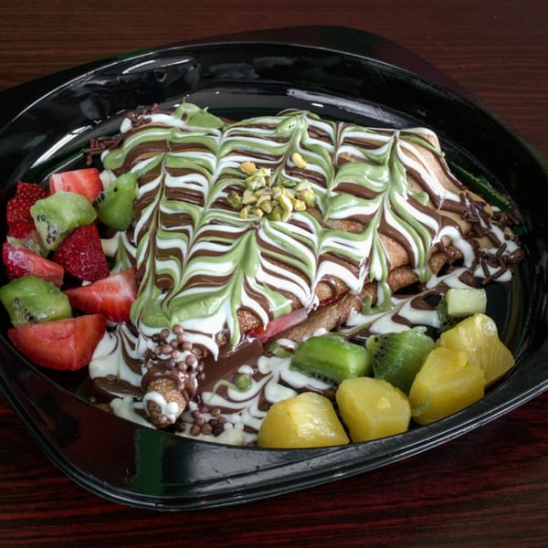 Ranoush dessert crepe drizzled with chocolate, pistachio, and white sauce, served with fresh fruit.