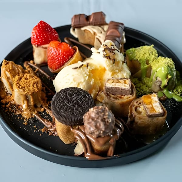 A black plate filled with Ranoush dessert crepes, ice cream, strawberries, and various candies.